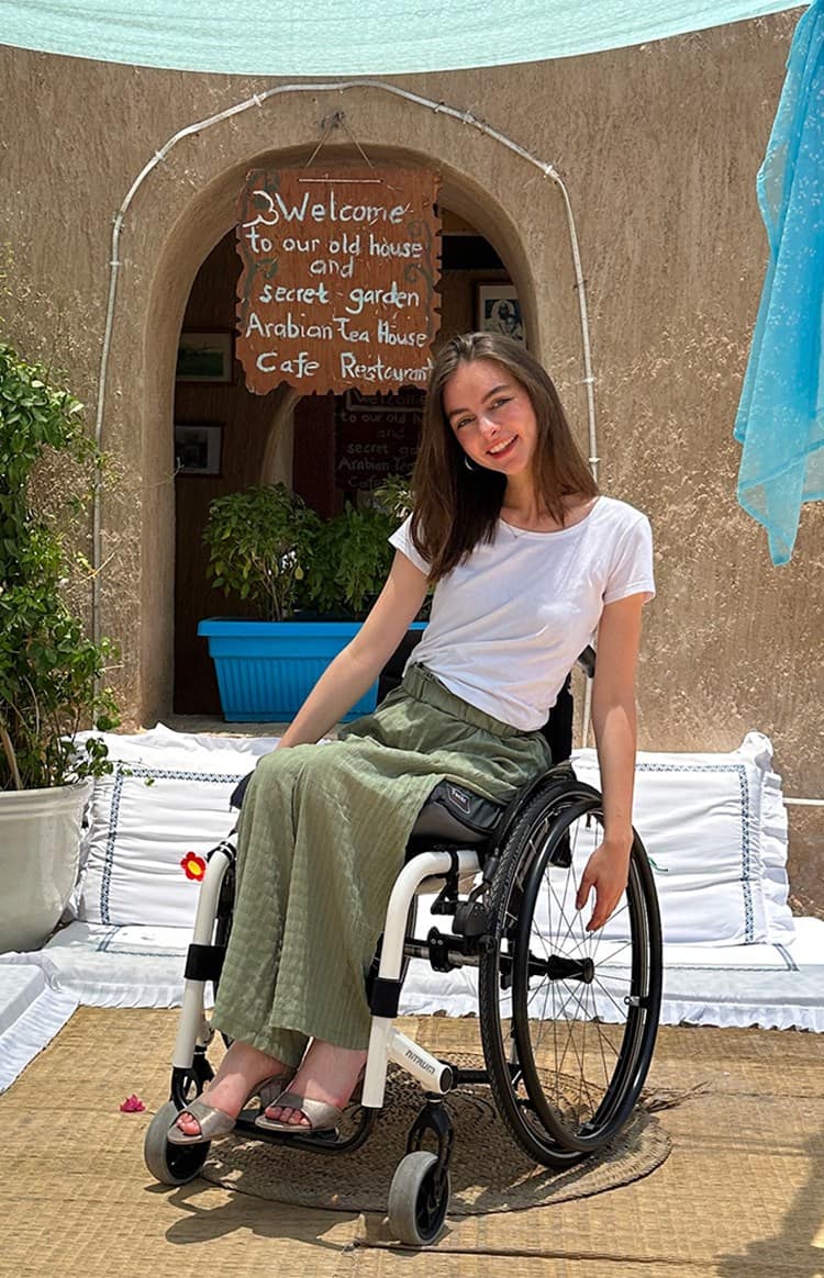 A smiling young woman on a wheelchair in a lounge with floor seat at the back