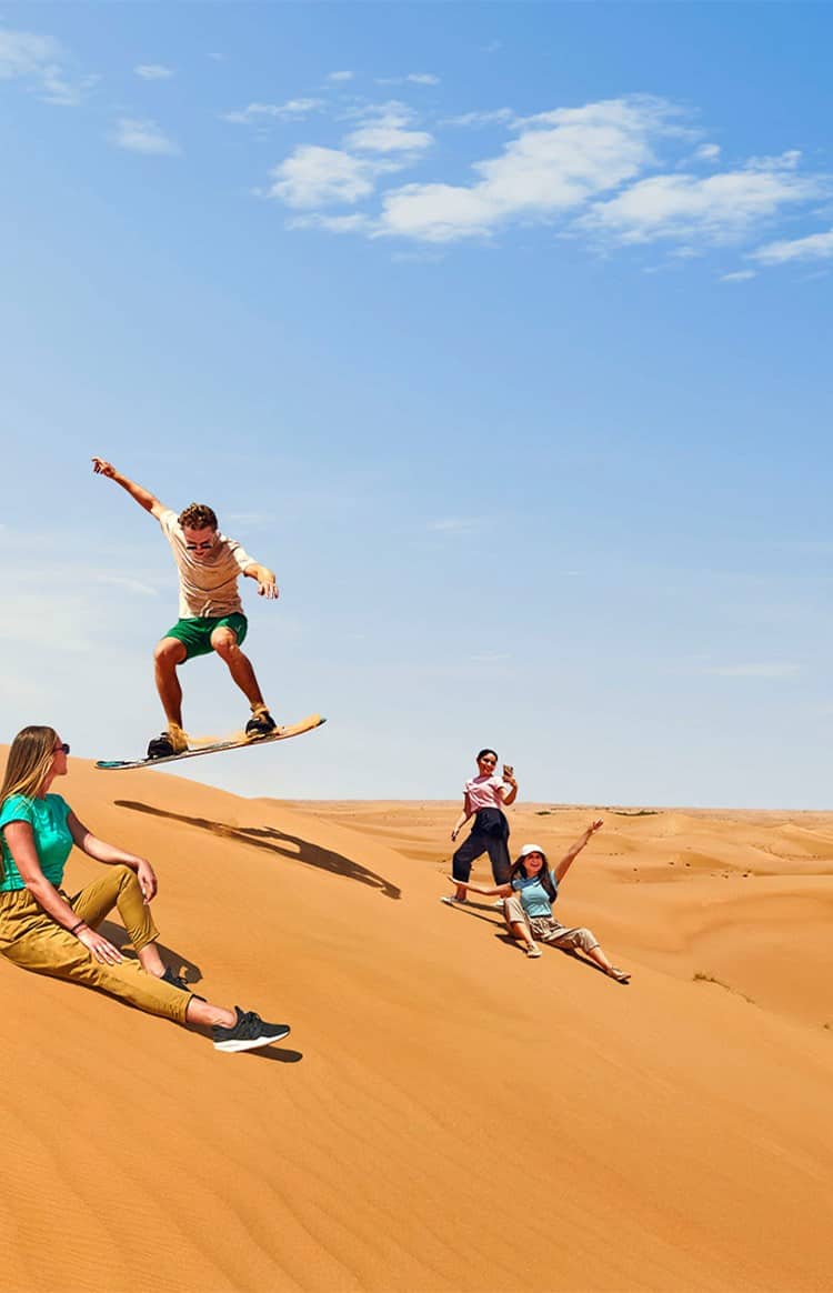 Group sandboarding on the dunes in the Dubai desert.